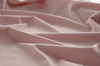 Yumuşak pembe bir kumaş düz bir yüzeyde hafifçe buruşmuş, doğal ışığı yakalıyor ve pürüzsüz dokusunu ve nazik kıvrımlarını vurguluyor, sakin bir atmosfer yaratıyor..