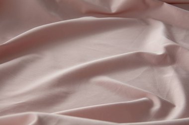 Yumuşak pembe bir kumaş düz bir yüzeyde hafifçe buruşmuş, doğal ışığı yakalıyor ve pürüzsüz dokusunu ve nazik kıvrımlarını vurguluyor, sakin bir atmosfer yaratıyor..