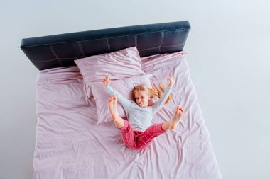 Genç bir kız pembe çarşaflar ve yastıklarla bir yatakta topun içinde kıvrılıyor. Parlak, havadar odada doğal ışık var. Sahneyi aydınlatıyor, sakin bir atmosfer yaratıyor..