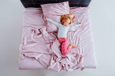 Genç kız pembe çarşaflar ve yastıklarla bir yatakta topun içinde kıvrılıyor. Parlak, havadar odada doğal ışık var. Sahneyi aydınlatıyor, sakin bir atmosfer yaratıyor..