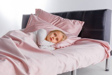 Küçük bir çocuk, rahat bir yatakta yumuşak pembe bir yatağa sarılı olarak huzur içinde uyuyor. Sabah ışığı odayı hafifçe aydınlatıyor, sakin bir atmosfer yaratıyor..