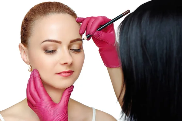 Beauty master correcting eyebrows shape with a brown cosmetic pencil