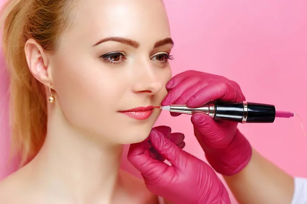 Closeup picture of lips tattooing procedure against pink background