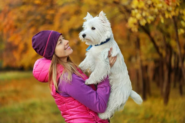 Woman lifting her white dog in the air