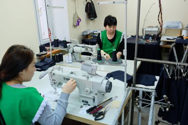 Almaty / Kazakistan - 04.09.2019: Şehir giyim üretiminde küçük işletme. Çalışanlar, mavi üniformaları ütülemek ve dikmek için desen hazırlıyorlar..