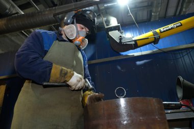 Almaty / Kazakistan - 08.18.2020: Bir fabrika işçisi metal ürünlerini yontmak için bir araç tutuyor. Düzenleyici materyal
