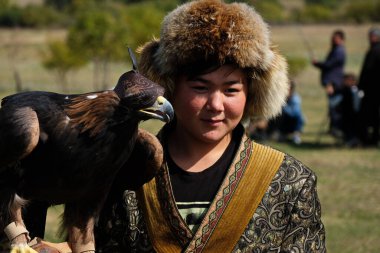 Almaty / Kazakistan - 09.23.2020: Kazak milli kostümlü bir genç elinde evcil bir altın kartal tutuyor.