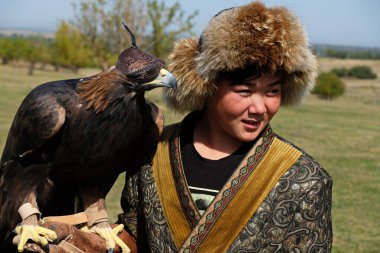 Almaty / Kazakistan - 09.23.2020: Kazak milli kostümlü bir genç elinde evcil bir altın kartal tutuyor.
