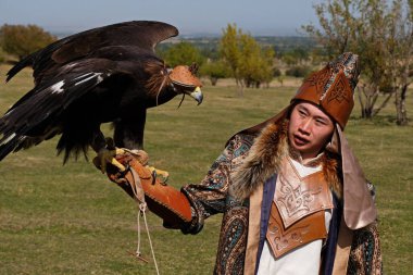 Almaty / Kazakistan - 09.23.2020: Kazak milli kostümlü bir genç elinde evcil bir altın kartal tutuyor.