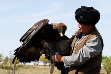 Almaty / Kazakistan - 09.23.2020: Kürk şapkalı ve ulusal elbiseli bir adam elinde evcil bir Altın Kartal tutuyor.