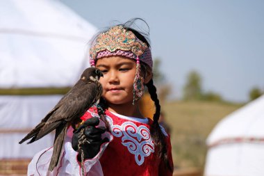 Almaty / Kazakistan - 09.23.2020: Kazak milli elbiseli küçük bir kız Balaban Şahinini kollarında tutuyor.