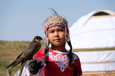 Almaty / Kazakistan - 09.23.2020: Kazak milli elbiseli küçük bir kız Balaban Şahinini kollarında tutuyor.