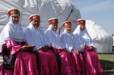 Almaty / Kazakistan - 09.23.2020: Kazak milli kostümlü yaşlı kadınlar arka arkaya bir bankta oturuyor.