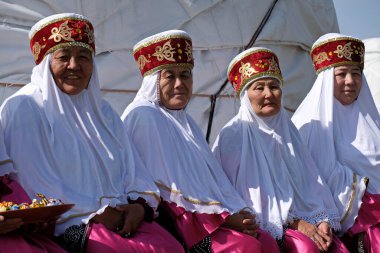 Almaty / Kazakistan - 09.23.2020: Kazak milli kostümlü yaşlı kadınlar arka arkaya bir bankta oturuyor.