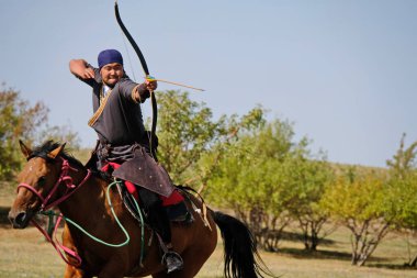 Almaty / Kazakistan - 09.23.2020: Yayı olan at üzerindeki ulusal kostümlü genç bir adam hedeflere ateş etmeyi öğreniyor.