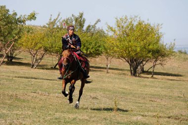 Almaty / Kazakistan - 09.23.2020: Elinde yay ve okla ulusal giysili bir genç, hedeflere ateş etmeyi öğreniyor.