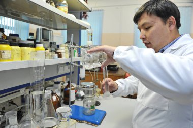 Almaty / Kazakistan - 05.07.2012: Bir tıp laboratuarı çalışanı analiz için cam şişelerden çeşitli sıvılar boşaltıyor.