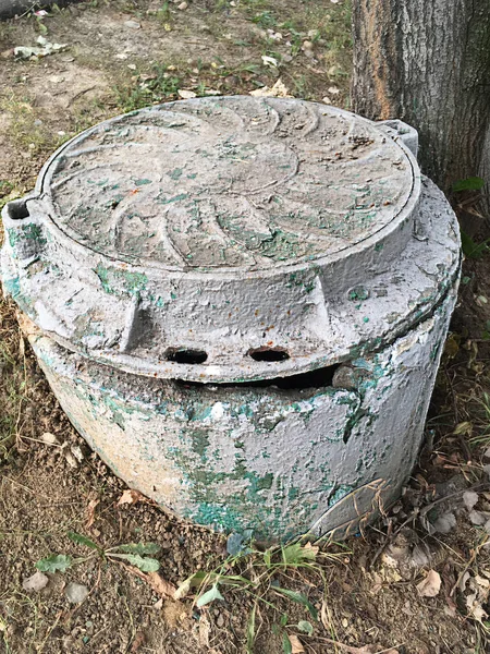 Kentsel yapıların bir unsuru olarak kahverengi, yeşil, gri boya katmanları ile kaplı harap bir rögar üzerinde eski kanalizasyon rögar,.