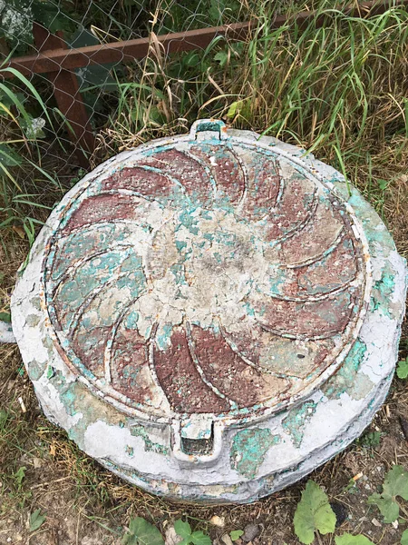 Kentsel yapıların bir unsuru olarak kahverengi, yeşil, gri boya katmanları ile kaplı harap bir rögar üzerinde eski kanalizasyon rögar,.