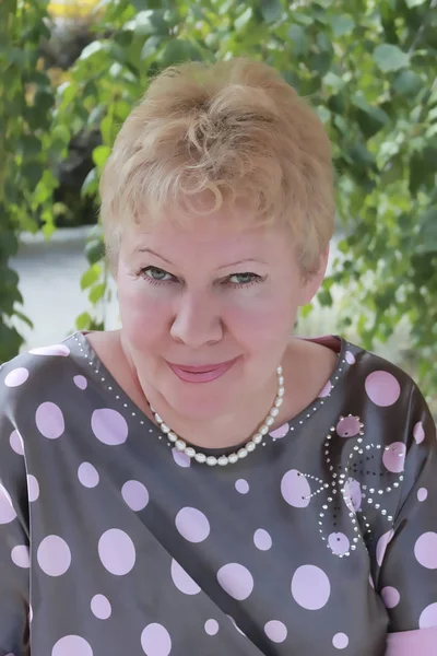 Olgun bir kadın ironik, yaz yeşil yeşillik bir arka plana karşı gülümsüyor