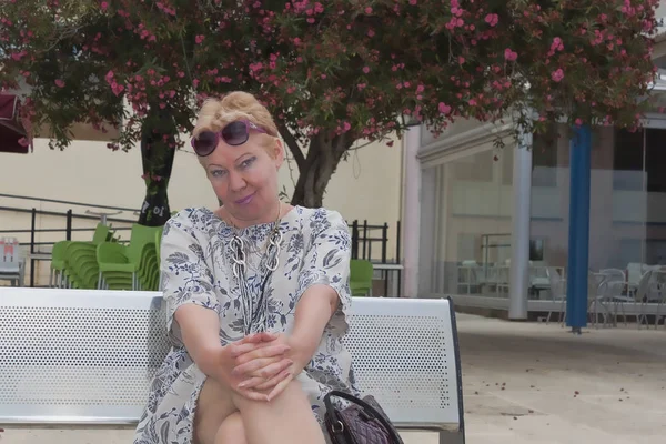 Pembe çiçekli bir ağacın altında bir bankta oturan olgun bir kadın portresi