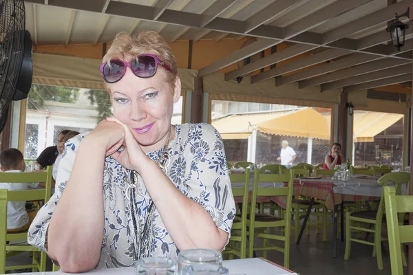 Bir yaz kafede bir masada oturan olgun bir kadın portresi