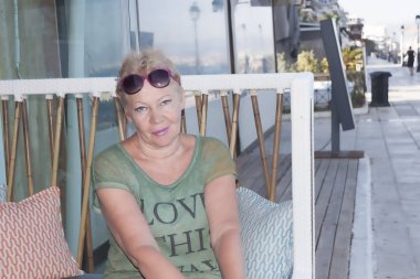 Bir kanepe yastıkları sahildeki Cafe tarafından ile olgun bir kadın portresi. Loutraki, Yunanistan