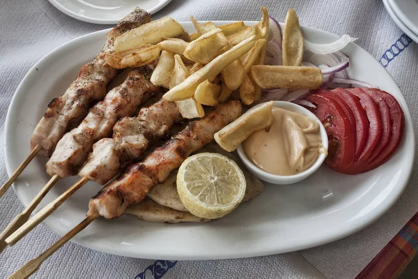 Traditional Greek food. Portion of souvlaki with fried potatoes, tomatoes, lemon and a saucepan