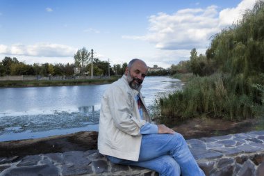 Yarı açık-bir göl arka plan üzerinde bir taş kaide üzerinde bir adam Olgun Yaş oturuyor