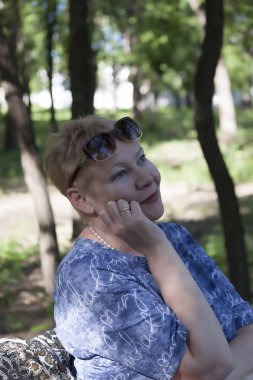 Bir bankta bir parkta oturan olgun bir kadının portresi