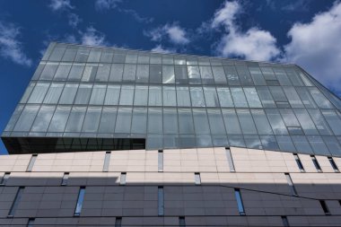 Cam ve betondan yapılmış yüksek bir bina. Bulutlu mavi gökyüzüne karşı aşağıdan çekilen