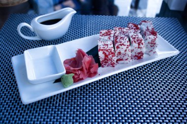 Beyaz dikdörtgen bir tabakta zencefilli, hardallı ve teriyaki soslu suşi.