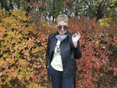 Sonbahar ormanında deri ceketli ve pantolonlu, olgun bir kadın.