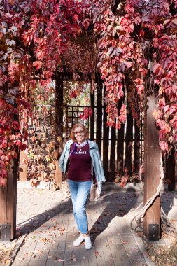 Kırmızı sarmaşık yapraklarıyla sarmalanmış çardağı olan olgun bir kadın.