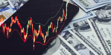 Yükselen bir şamdan şemasını gösteren mobil cihaz, kar, finans ve yatırımı sembolize eden dağınık yüz dolarlık banknotların üzerinde yer alıyor..