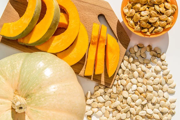 Toasted pumpkin seeds with raw seeds and pumpkin on a white table. — Stock Photo, Image