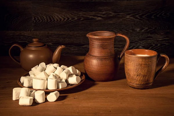 白棉花糖 粘土壶 茶壶和一杯牛奶在一张木桌上 美丽的黑暗背景 — 图库照片