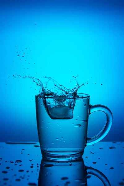 Splash Água Uma Xícara Fundo Azul — Fotografia de Stock