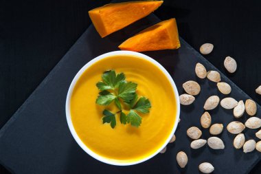 Balkabağı çorbası ve kabak çekirdeği bir siyah ahşap tablo.