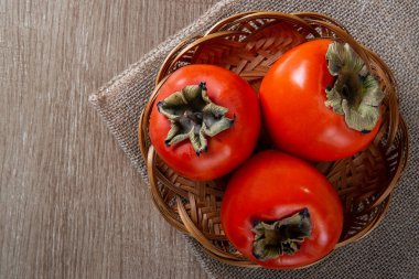 Çuval bezi üzerinde ahşap bir masa üzerinde bir sepet içinde Trabzon hurması.