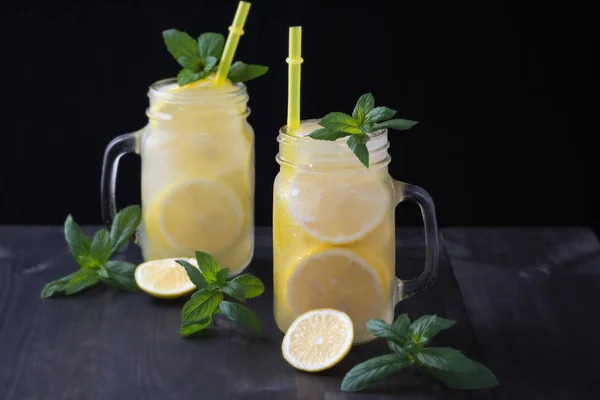Lemonade in a jar with ice and mint on a black wooden table.