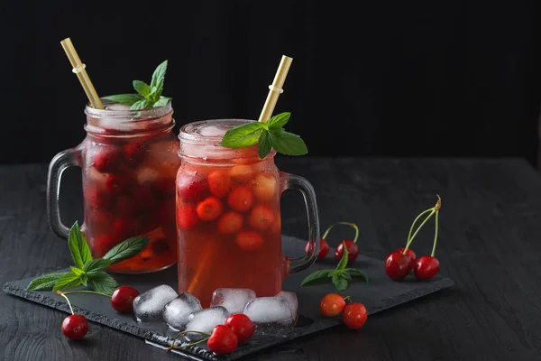 Fresh summer cocktail with sweet cherry and ice cubes on a dark background on a black wooden table. — Stock Photo, Image