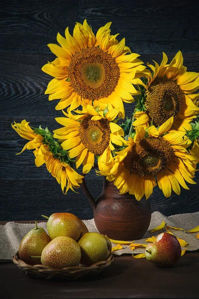 Nature morte avec des tournesols dans un pot d'argile et des poires sur le fond d'un mur en bois . — Photo