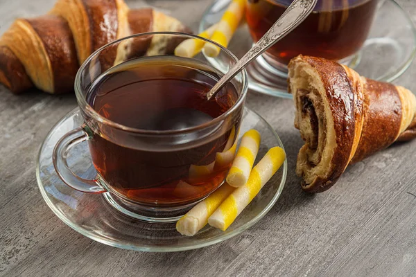 Kaffee in einer durchsichtigen Tasse und Croissants auf einem Holztisch. — Stockfoto