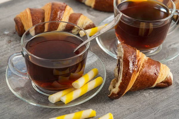 Kaffee in einer durchsichtigen Tasse und Croissants auf einem Holztisch. — Stockfoto