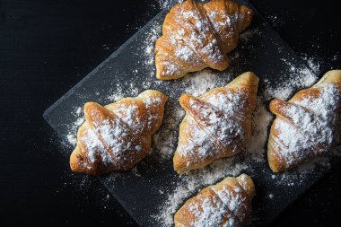 Taze kruvasan siyah bir masaya şeker serpilir.