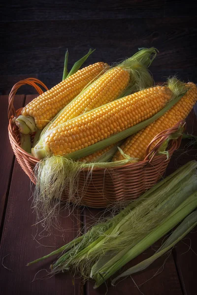 Fresh corn on the cob in wicker basket on brown wooden table. — Stock Photo, Image