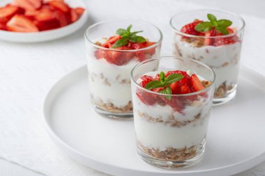 Tahıllı yoğurt ve beyaz bir masada cam içinde çilek.