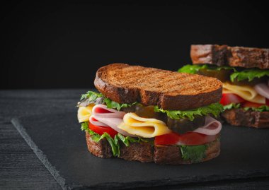 Sandwich with ham, cheese, tomatoes, lettuce, and toasted bread.	