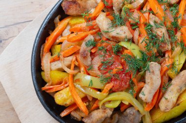 Hafif ahşap bir masada tavada sebzeli et.